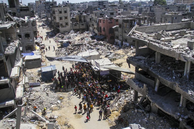 reúnen entorno a una cocina solidaria para consumir alimentos calientes, cerca de las ruinas de las casas destruidas durante la ofensiva israelí, en Jabalia, en el norte de la Franja de Gaza.