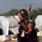 Madre portando a un niño en un campo de personas refugiadas en Siria.
