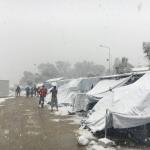 Varios refugiados entre las tiendas de campaña cubiertas de nieve del campo de personas refugiadas de Moria.