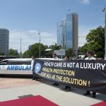 Miembros de Médicos del Mundo reclaman el derecho universal a la salud junto a una limusina con el rótulo "ambulancia"