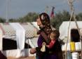 Madre portando a un niño en un campo de personas refugiadas en Siria.